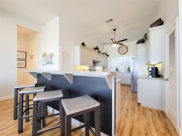 kitchen with a kitchen bar, light wood-style flooring, a ceiling fan, visible vents, and light countertops