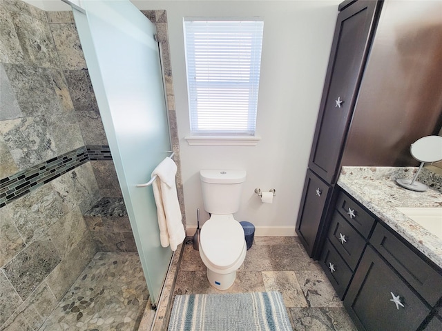 bathroom with vanity, baseboards, a stall shower, toilet, and stone tile flooring