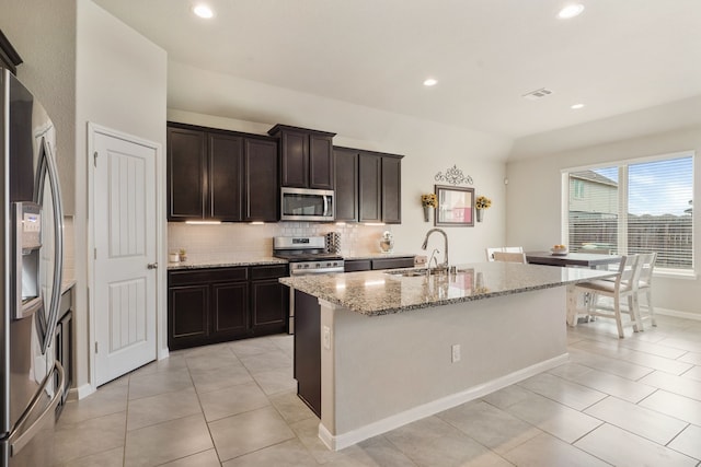 kitchen with stainless steel appliances, visible vents, backsplash, a sink, and light stone countertops