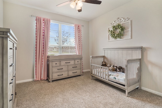 carpeted bedroom featuring a crib, a ceiling fan, and baseboards