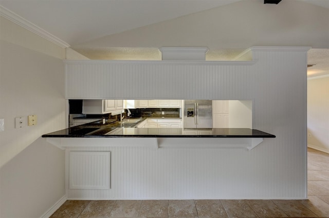 kitchen with a peninsula, vaulted ceiling, stainless steel refrigerator with ice dispenser, and a sink