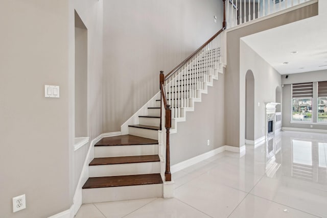 stairs with tile patterned floors, a fireplace, baseboards, and a towering ceiling