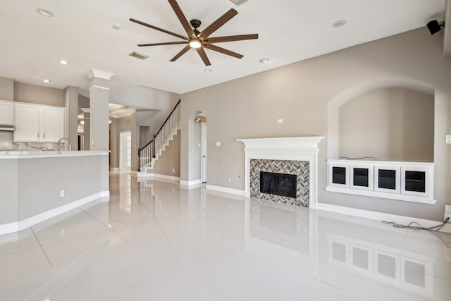 unfurnished living room with visible vents, a sink, recessed lighting, stairs, and a tile fireplace