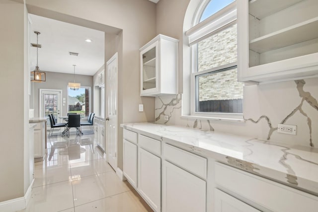 kitchen featuring visible vents, pendant lighting, light stone counters, white cabinetry, and glass insert cabinets