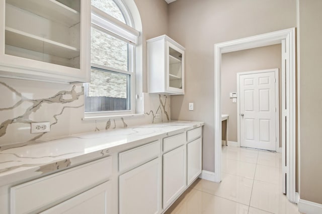 kitchen with baseboards, white cabinets, light tile patterned floors, glass insert cabinets, and light stone countertops