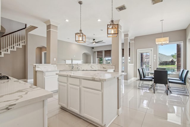 kitchen featuring visible vents, a kitchen island, pendant lighting, white cabinets, and a sink