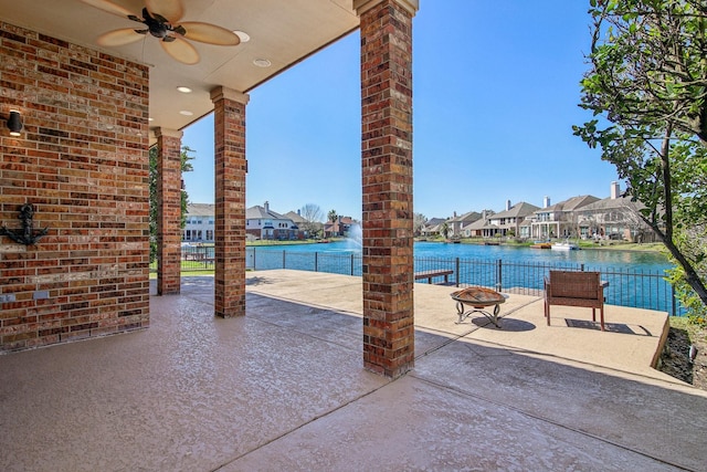 view of patio featuring fence, an outdoor fire pit, ceiling fan, a water view, and a residential view