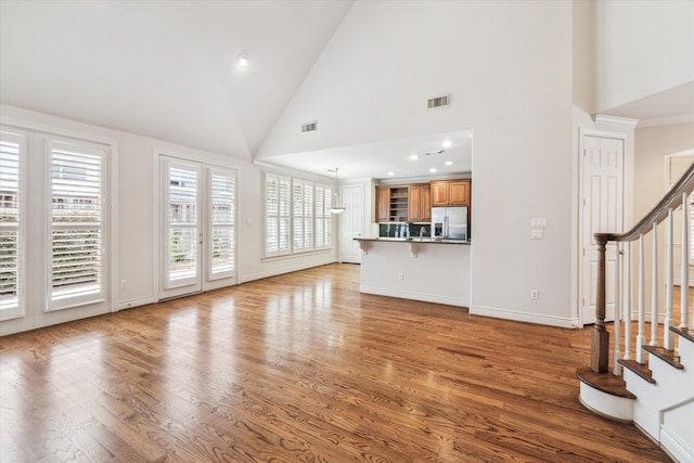 unfurnished living room with high vaulted ceiling, stairway, light wood-type flooring, and visible vents