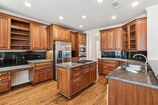 kitchen featuring light wood-style flooring, stainless steel appliances, a sink, built in study area, and brown cabinetry