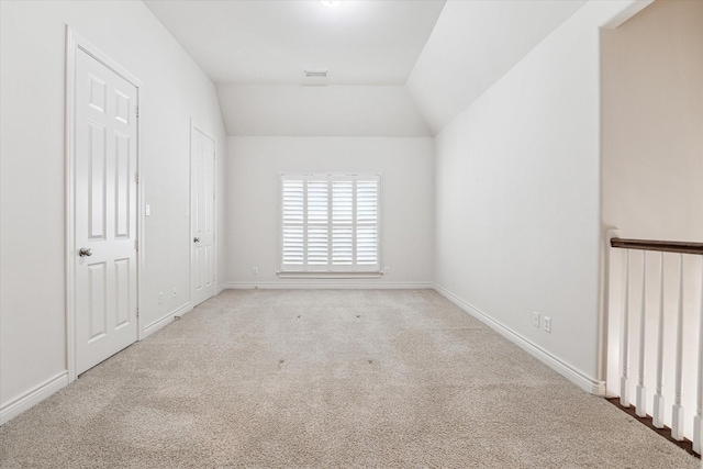 unfurnished room featuring lofted ceiling, light colored carpet, visible vents, and baseboards