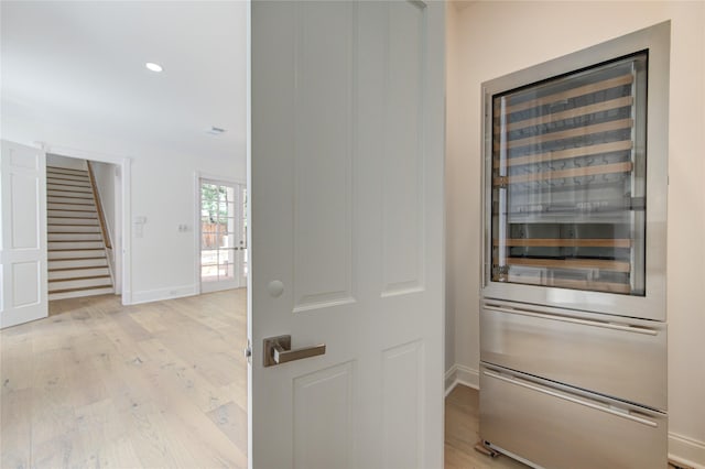 corridor with beverage cooler, baseboards, light wood-style flooring, stairway, and recessed lighting