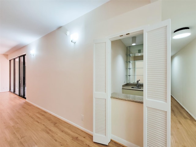 hallway with light wood-type flooring, a sink, and baseboards