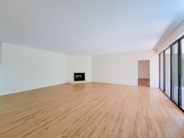 unfurnished living room with light wood-style floors and a fireplace with raised hearth