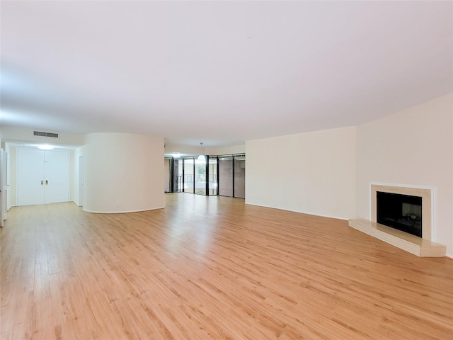 unfurnished living room with a fireplace with raised hearth, light wood finished floors, a wall of windows, and visible vents