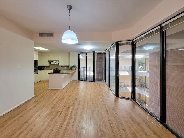 kitchen featuring a peninsula, light wood-type flooring, visible vents, and decorative light fixtures