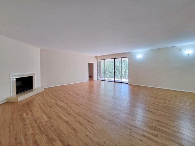 unfurnished living room with light wood finished floors, baseboards, and a fireplace with raised hearth