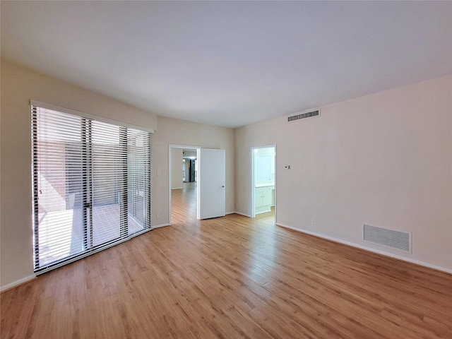 spare room featuring light wood finished floors, visible vents, and baseboards