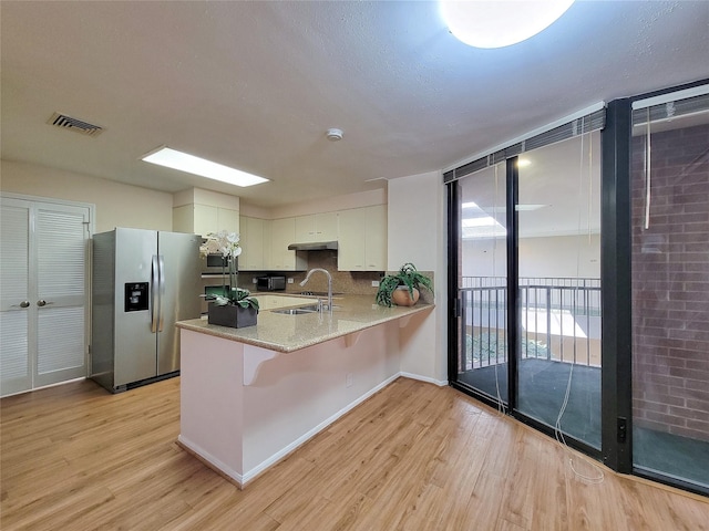 kitchen with light wood-style flooring, stainless steel appliances, a peninsula, a sink, and white cabinets