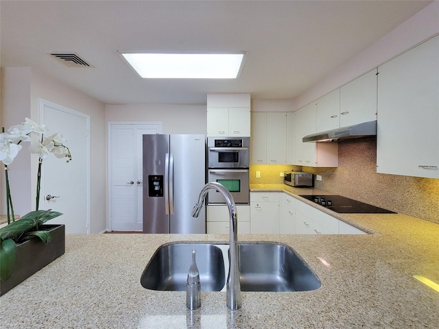 kitchen with under cabinet range hood, a sink, white cabinets, appliances with stainless steel finishes, and backsplash