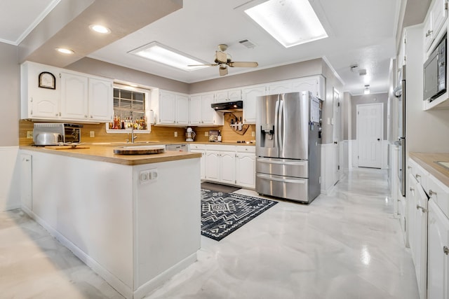 kitchen featuring backsplash, white cabinets, a peninsula, stainless steel fridge, and under cabinet range hood