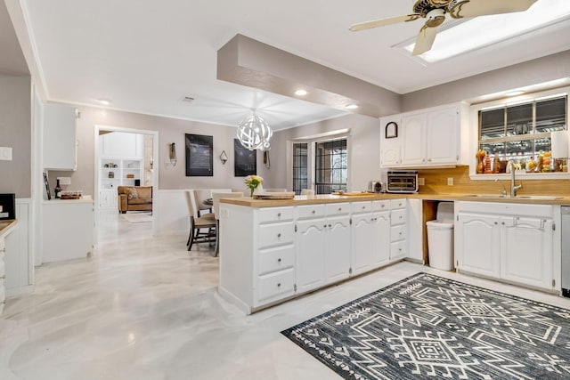 kitchen with white cabinets, a peninsula, light countertops, backsplash, and ceiling fan with notable chandelier