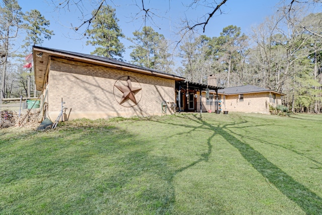 rear view of property featuring a yard, brick siding, and a chimney