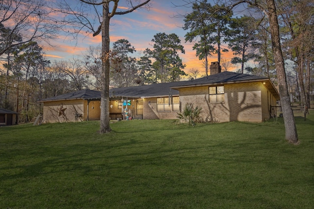 back of property at dusk featuring brick siding, a lawn, and a chimney