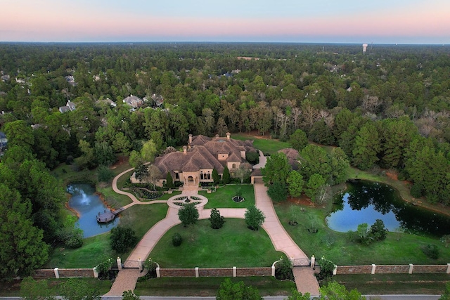 aerial view at dusk with a water view and a wooded view