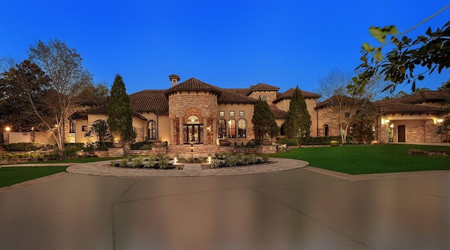 mediterranean / spanish-style house featuring a tiled roof, stone siding, a front yard, and stucco siding