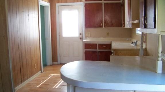 kitchen featuring light wood finished floors, light countertops, a sink, wooden walls, and baseboards