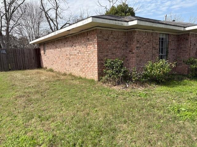 view of property exterior featuring fence, a lawn, and brick siding