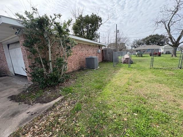 view of yard with a gate, fence, central AC, and concrete driveway