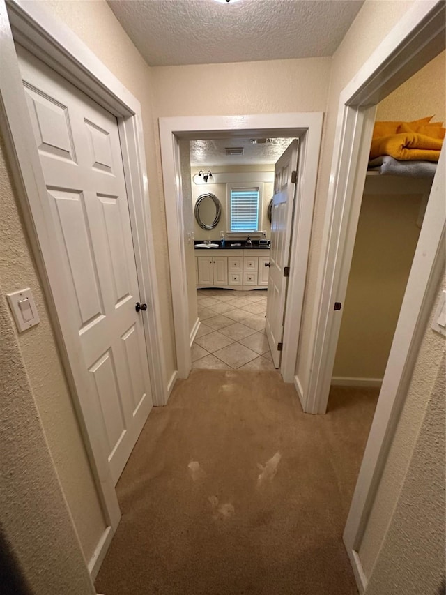 hallway featuring a textured ceiling, baseboards, and light colored carpet