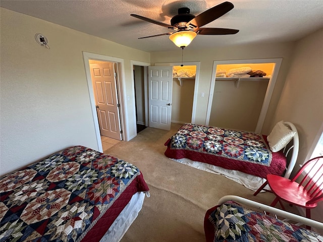 bedroom featuring light carpet, ceiling fan, a textured ceiling, and multiple closets