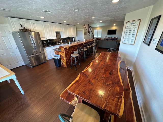 kitchen featuring dark wood-type flooring, freestanding refrigerator, white cabinetry, and tasteful backsplash