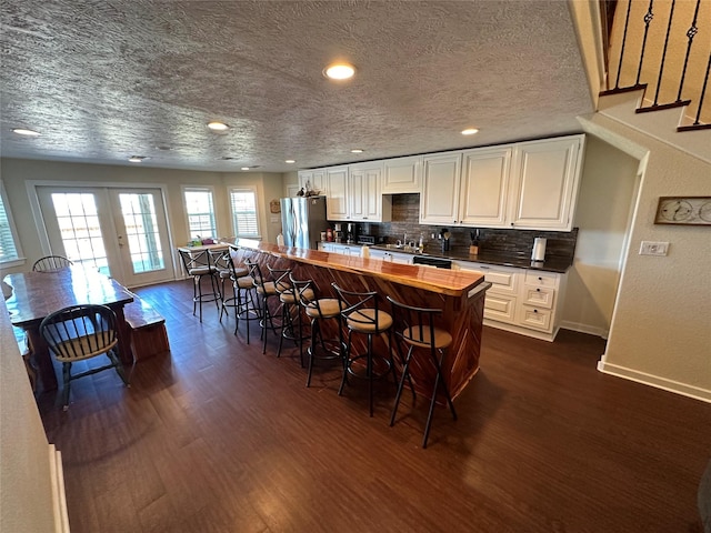 kitchen featuring a breakfast bar, french doors, backsplash, freestanding refrigerator, and dark wood-style floors