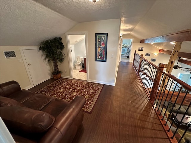 interior space featuring a textured ceiling, wood finished floors, visible vents, baseboards, and vaulted ceiling