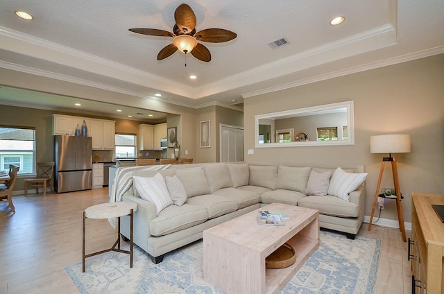 living room featuring light wood finished floors, visible vents, a raised ceiling, a ceiling fan, and recessed lighting