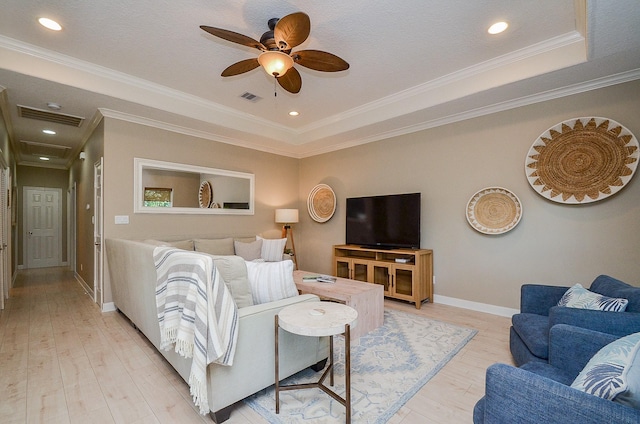 living room featuring visible vents, baseboards, light wood-type flooring, a tray ceiling, and crown molding