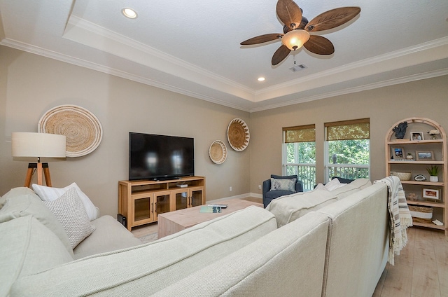 living area featuring a tray ceiling, crown molding, light wood finished floors, visible vents, and ceiling fan