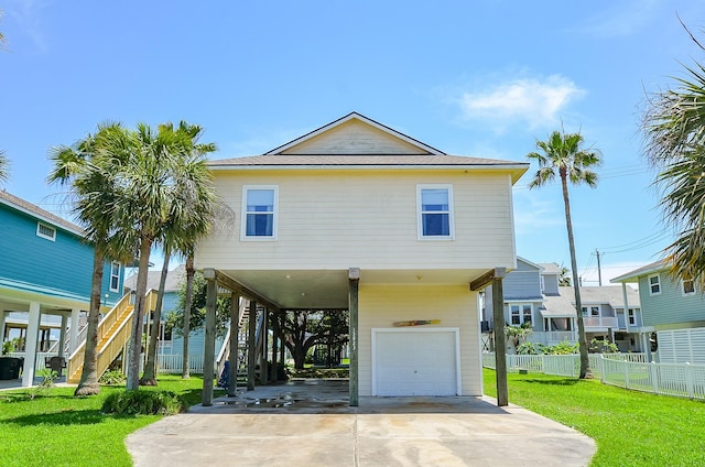 coastal inspired home with concrete driveway, a front yard, fence, a carport, and stairs