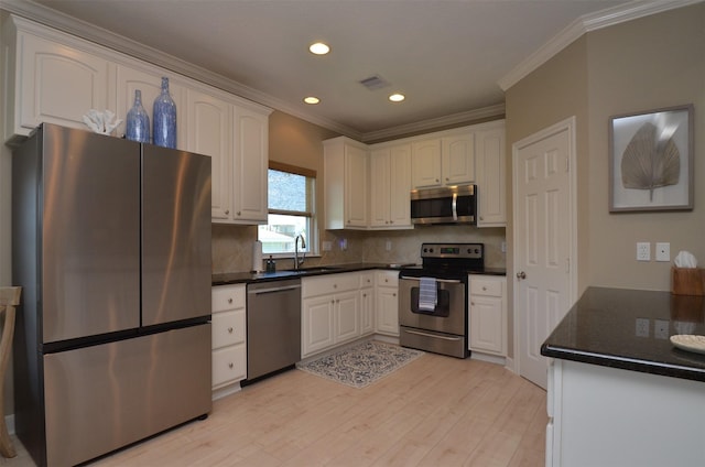 kitchen featuring light wood finished floors, stainless steel appliances, visible vents, white cabinets, and a sink