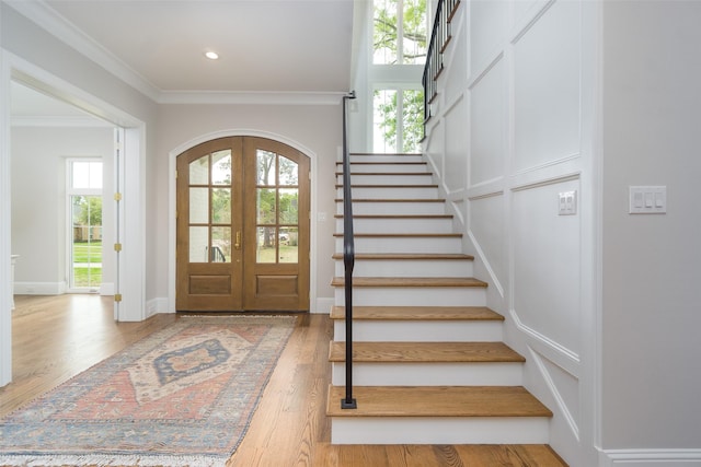 entrance foyer with arched walkways, wood finished floors, ornamental molding, french doors, and stairway