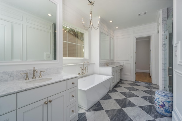 full bath featuring two vanities, visible vents, a freestanding bath, an inviting chandelier, and a sink