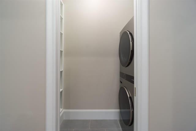 clothes washing area with stacked washer / drying machine, laundry area, baseboards, and tile patterned floors