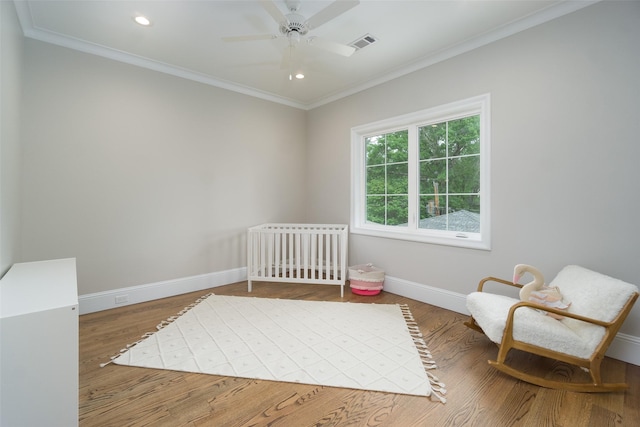 bedroom with a crib, baseboards, visible vents, ornamental molding, and wood finished floors