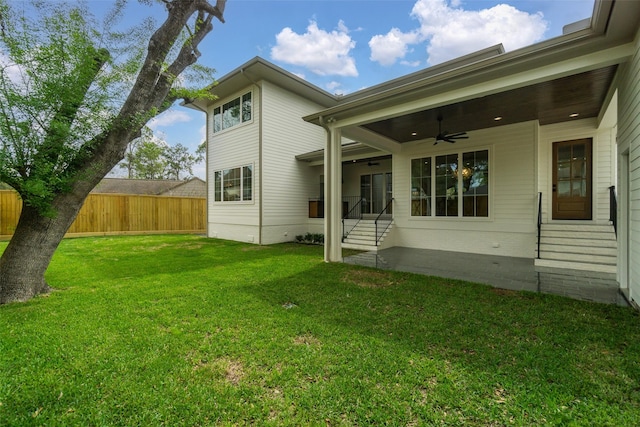 rear view of property with entry steps, fence, a ceiling fan, and a yard