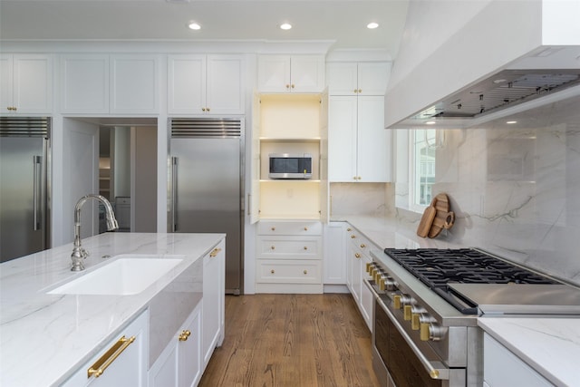 kitchen with white cabinets, a sink, wood finished floors, high quality appliances, and wall chimney exhaust hood