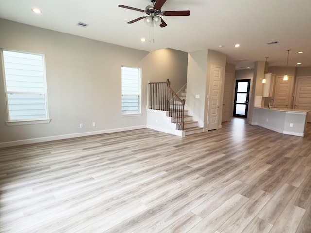 unfurnished living room with a wealth of natural light, recessed lighting, light wood-type flooring, baseboards, and stairs