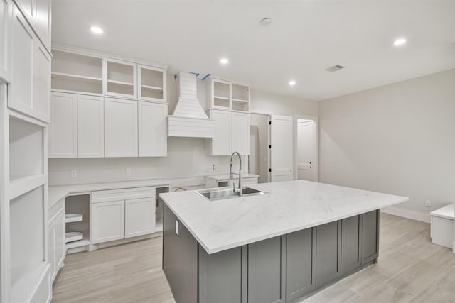 kitchen with a center island with sink, light wood-type flooring, premium range hood, open shelves, and a sink